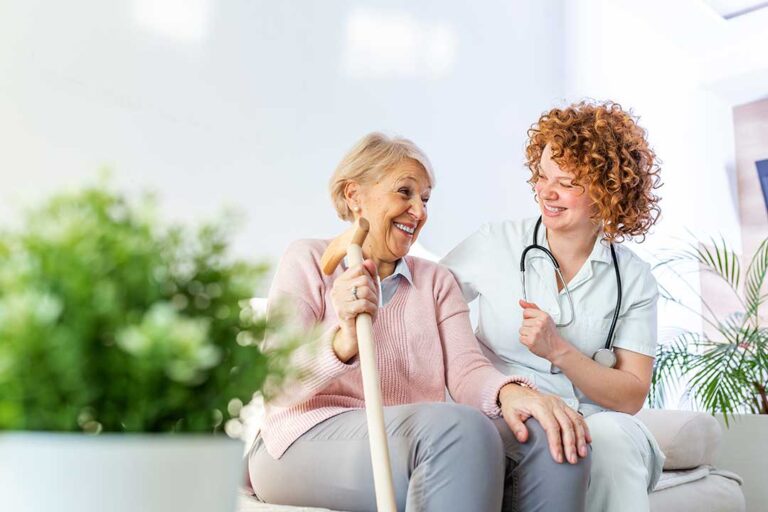 Older adult choosing clothing beside a caregiver in a bright assisted living room.